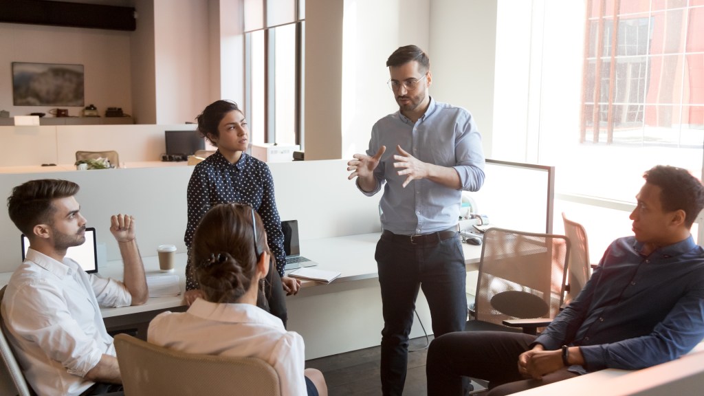 Serious business man team leader coach mentor talk to diverse business people in office explain strategy at corporate group meeting, multiethnic staff listen to boss instruct interns at briefing