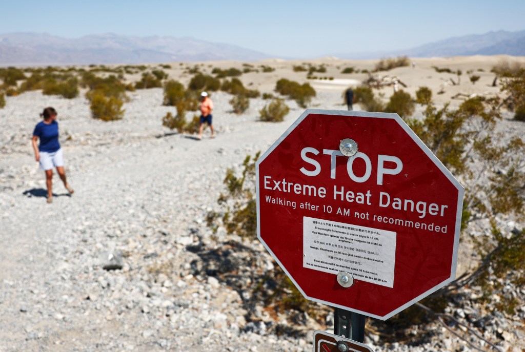 Visitors walk near a 'Stop Extreme Heat Danger' sign at Mesquite Flat Sand Dunes in the morning, when temperatures are less hot, during a long-duration heat wave which is impacting much of California on July 9, 2024 in Death Valley National Park, California.