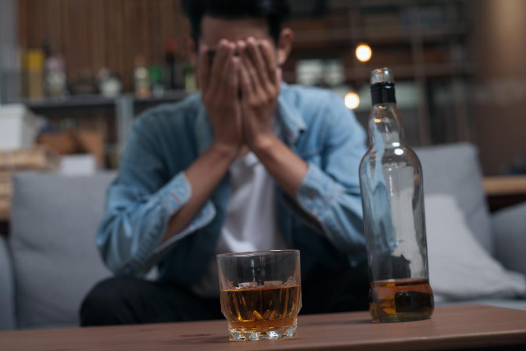 Close-up of a young Asian man looking depressed, drinking alcohol alone in a pub due to stress and life problems