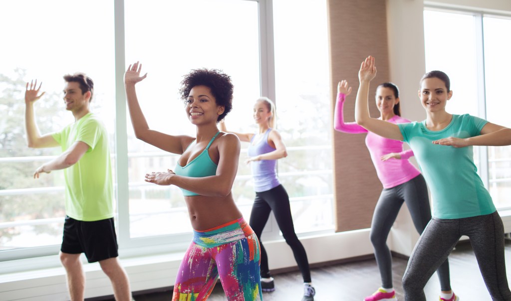 Group of smiling people with coach, dancing Zumba in a fitness studio