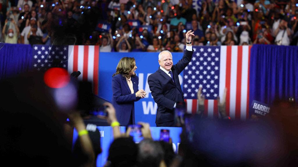 Governor Tim Walz making remarks at a campaign event after being introduced by Vice President Kamala Harris as her Vice Presidential nominee, both waving at the crowd.