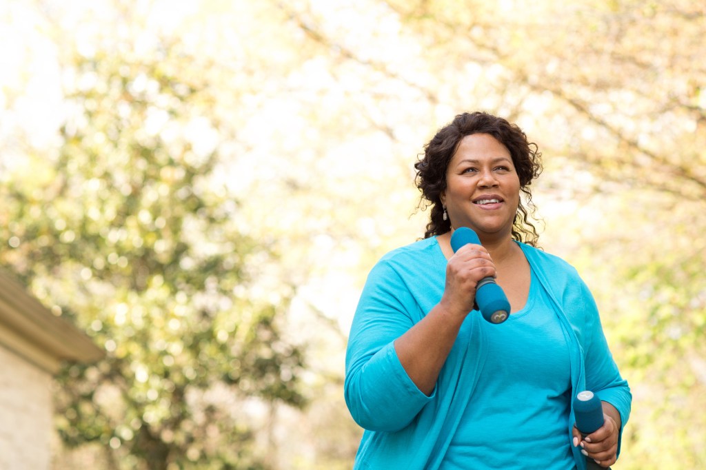 Mature African American woman smiling and holding weights