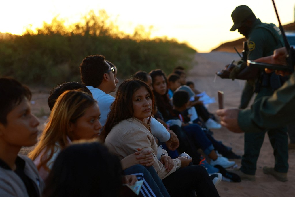 A group of migrants sit before border agents, who are processing them for apprehension.