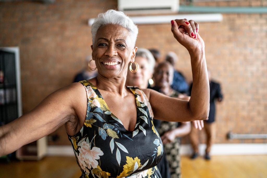 Senior woman joyfully dancing with friends in a dance hall with her arm raised