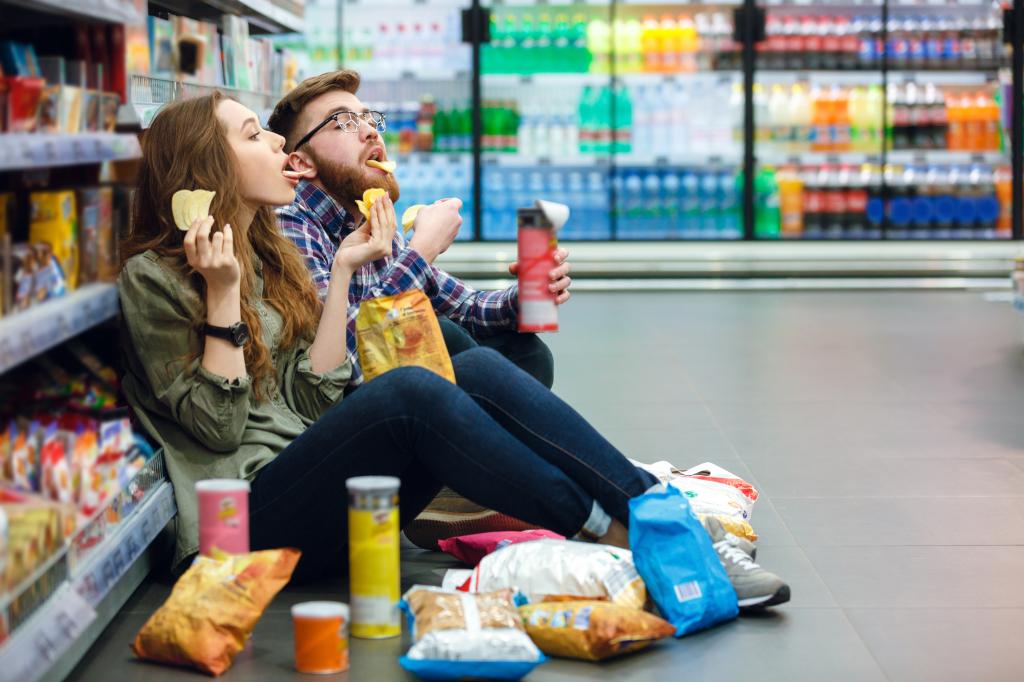 Young couple sitting on supermarket floor eating junk food