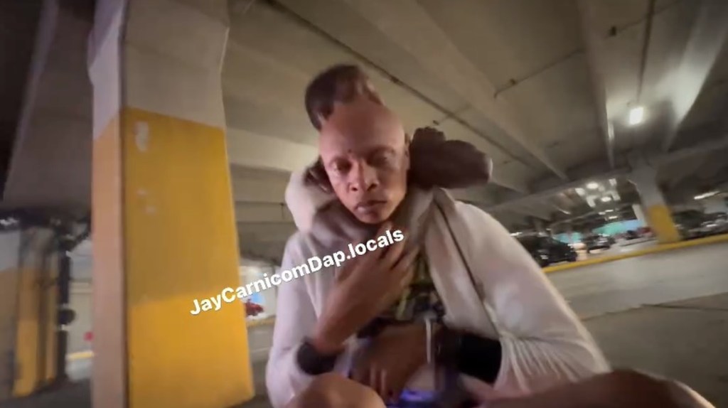 Man being held in a chokehold by another man, in a parking garage