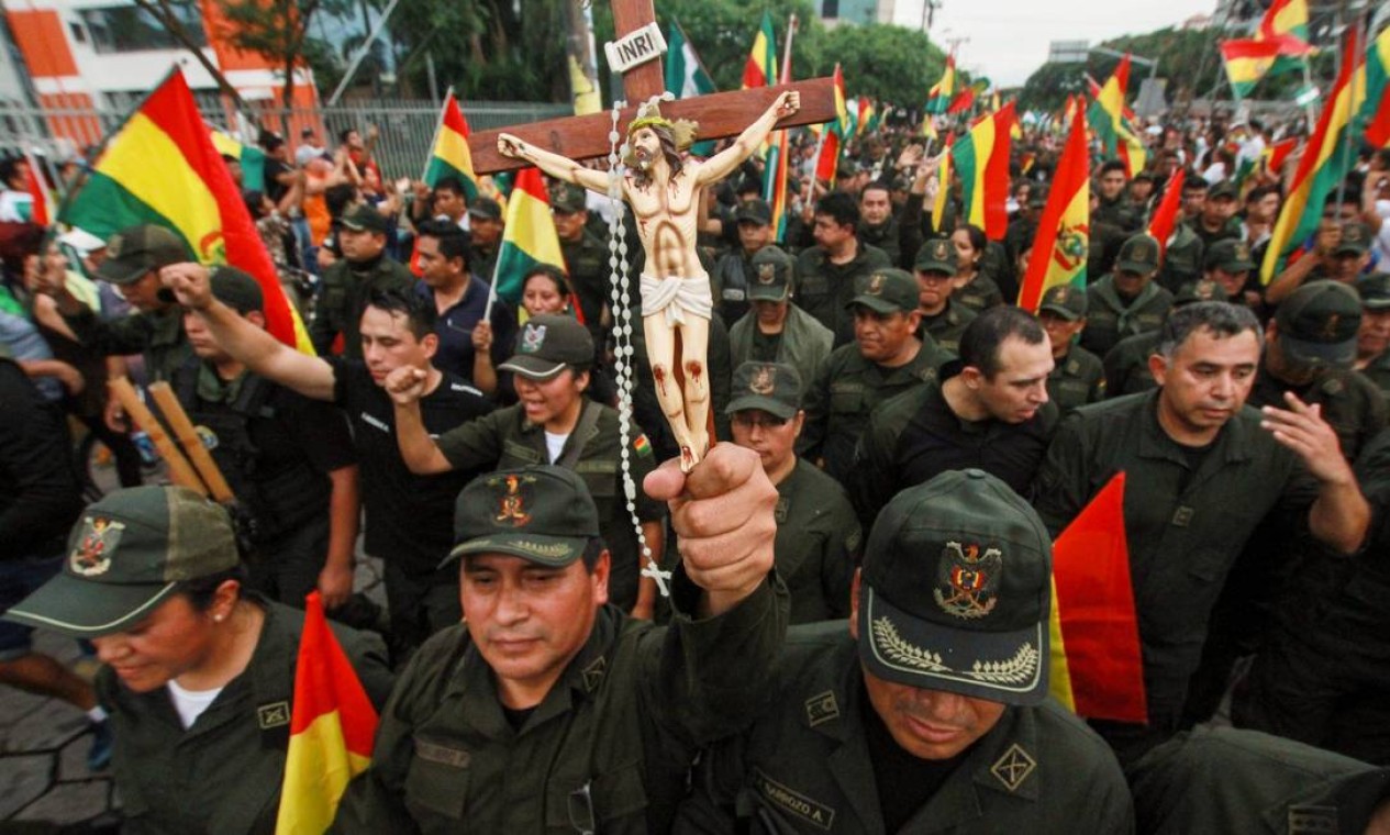 Oficial da polícia carrega crucifixo em desfile em comemoração à renúncia do presidente, em Santa Cruz de La Sierra, reduto oposicionista Foto: Daniel Walker / AFP