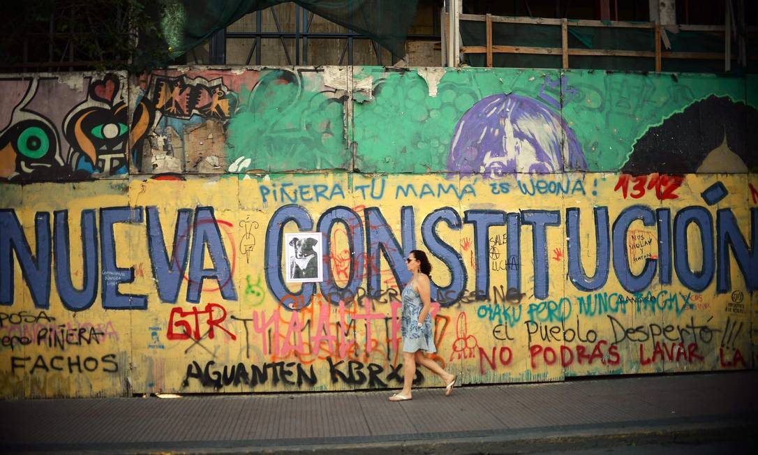 Mulher passa diante de muro pedindo nova constituição em Santiago. Nova Carta, substituindo o texto de 1980, é demanda frequente nos protestos Foto: RODRIGO ARANGUA / AFP