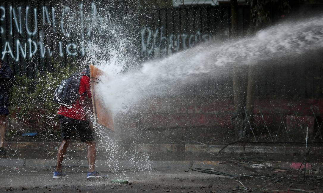 Manifestante usa pedaço de madeira para enfrentar canhão de água durante protesto em Santiago. ONU recomenda que forças de segurança do país adotem abordagem menos violenta nas ruas Foto: RICARDO MORAES / REUTERS