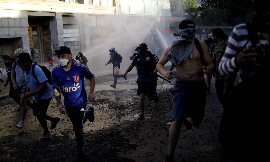 Manifestantes fogem enquanto polícia de choque dispara canhão de água durante protesto contra o governo, em Santiago Foto: ANDRES MARTINEZ CASARES / REUTERS
