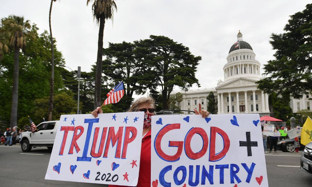 Simpatizante do presidente Donald Trump segura cartazes: um diz "Deus + País"; outro faz trocadilho entre o nome do presidente e a palavra "triunfo" Foto: JOSH EDELSON / AFP