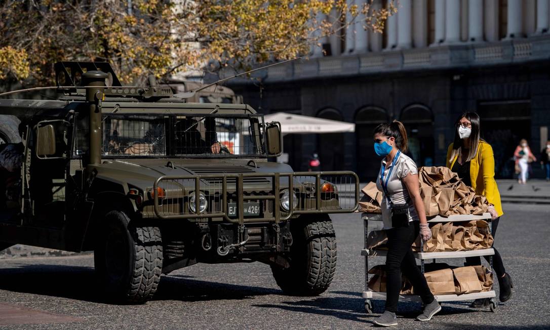 Mulheres carregam um carrinho com comida em frente a um veículo militar na Plaza de Armas, em Santiago, onde a quarentena será endurecida Foto: MARTIN BERNETTI / AFP
