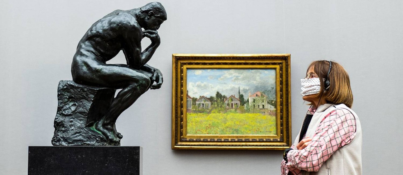 Uma vistante de máscara olha a uma versão em mármore e bronze de 'O pensador', assinada por Auguste Rodin, na Alte Nationalgalerie de Berlim, reaberta no dia 12 Foto: JOHN MACDOUGALL / AFP