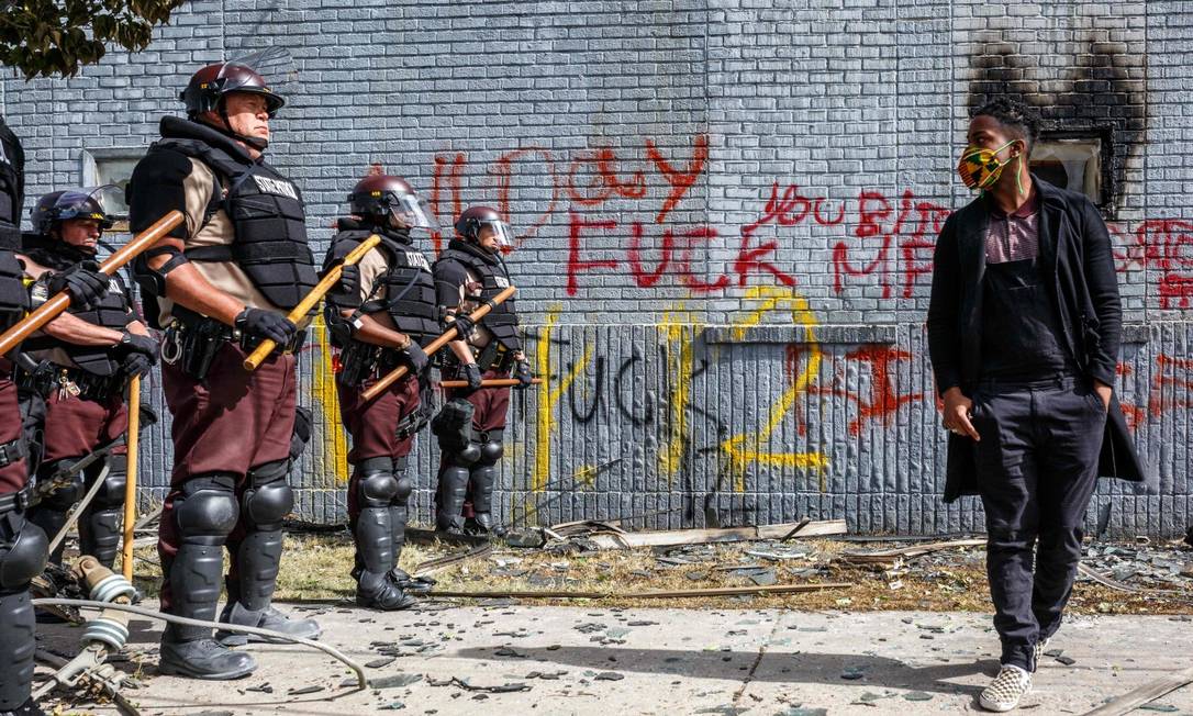 De máscara, manifestante contra a morte de George Floyd se posiciona frente à polícia de Minneapolis Foto: KEREM YUCEL / AFP