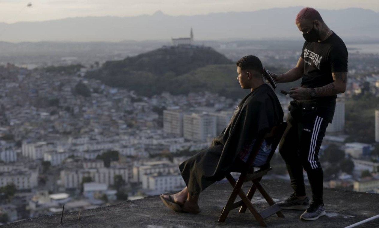 Barbeiro "delivery". Renan Estate corta o cabelo de morador do Alemão em cima de uma laje. Após o isolamento social, ele passou a atender em domicílo e ficou surpreso com a procura. Ele ainda aceita
como pagamento mantimentos, que
distribui entre vizinhos do complexo Foto: Domingos Peixoto / Agência O Globo - 25/06/2020