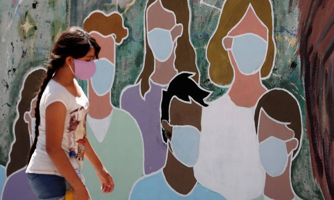 Em Buenos Aires, na Argentina, menina caminha em frente de mural com grafite de pessoas com máscaras Foto: AGUSTIN MARCARIAN / REUTERS
