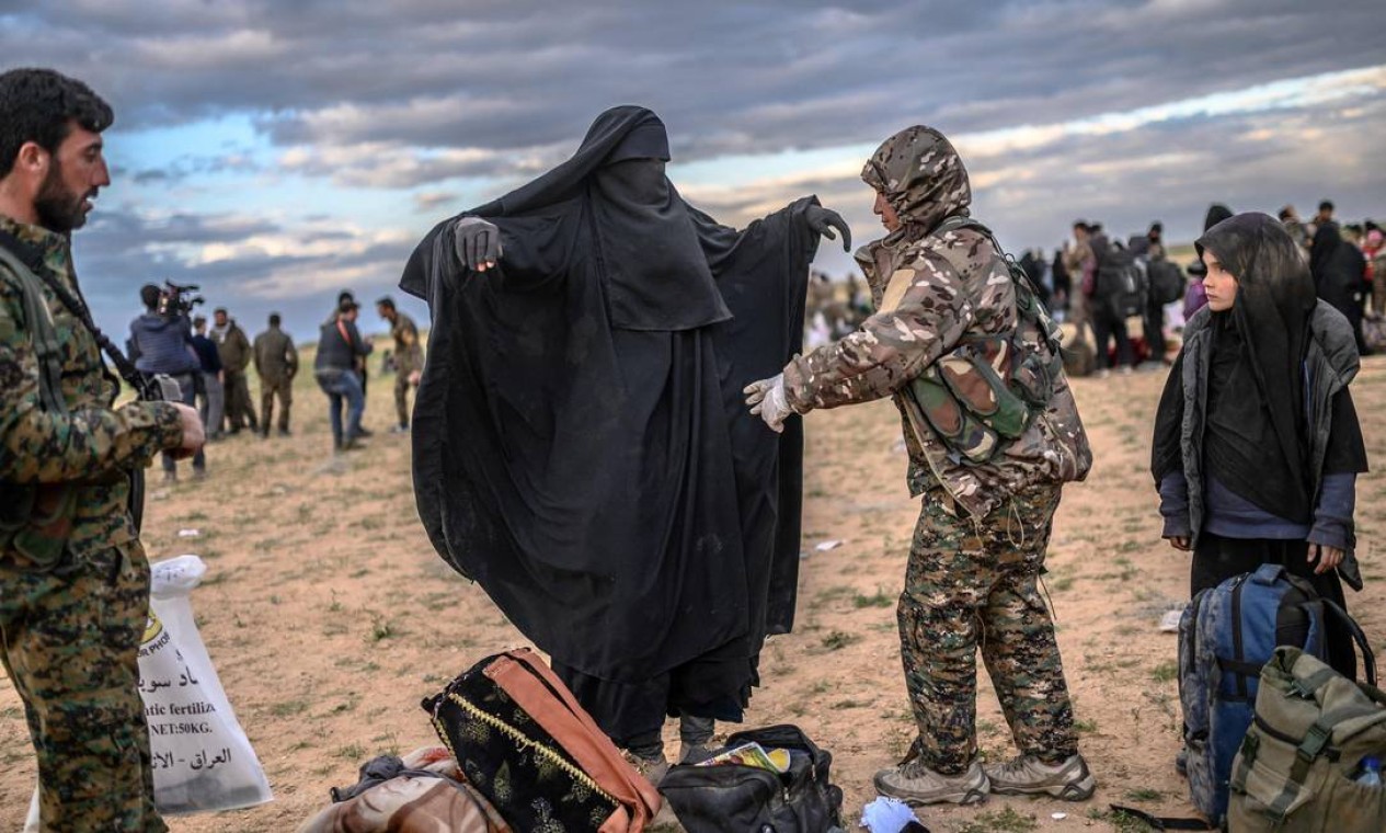 Membro das Forças Democráticas Sírias lideradas por curdos (SDF) revista uma mulher depois que ela deixou o último reduto do grupo IS em Baghouz, na província de Deir Ezzor, no norte da Síria Foto: BULENT KILIC / AFP - 27/02/2019