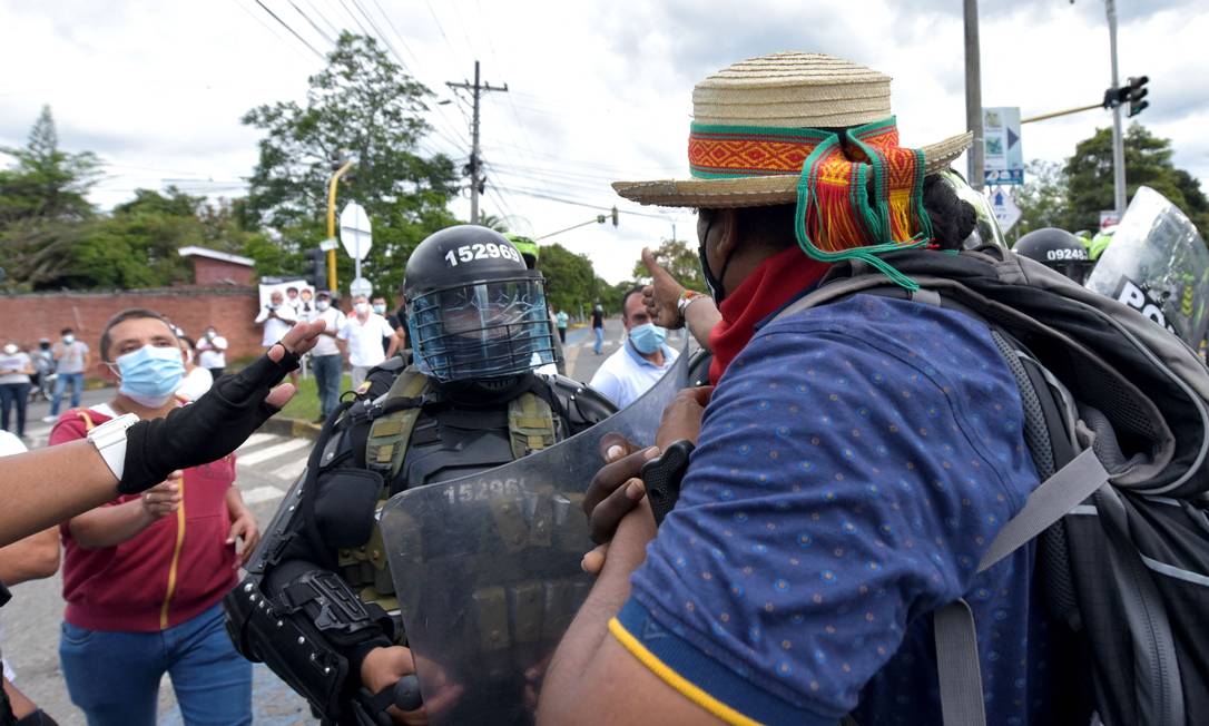 Um policial se posiciona entre indígenas e manifestantes que se opõem a bloqueios durante protestos em Cali, Colômbia Foto: LUIS CARLOS AYALA / AFP
