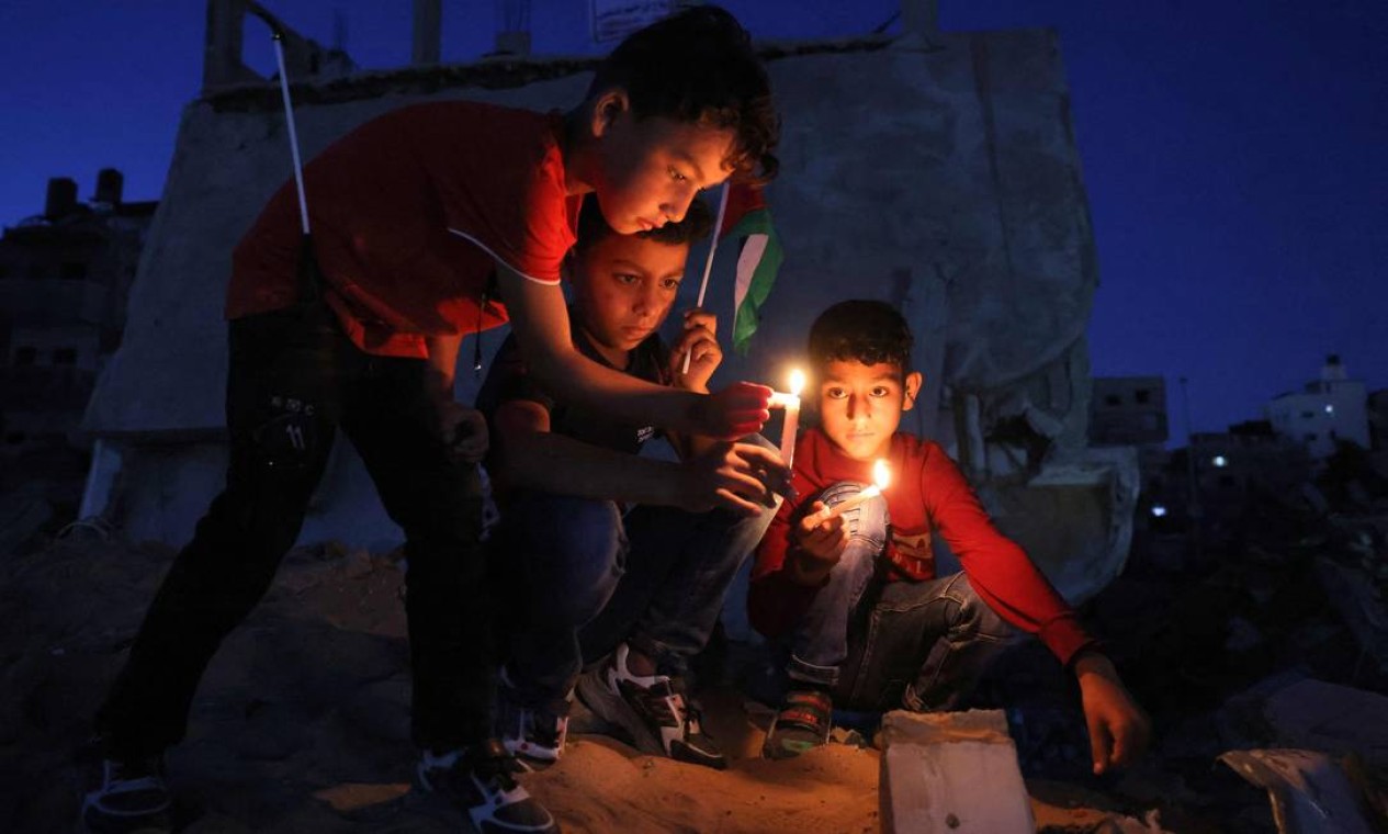 Crianças palestinas acendem velas durante um ato em meio às ruínas de casas destruídas por ataques israelenses, na Cidade de Gaza Foto: MOHAMMED ABED / AFP