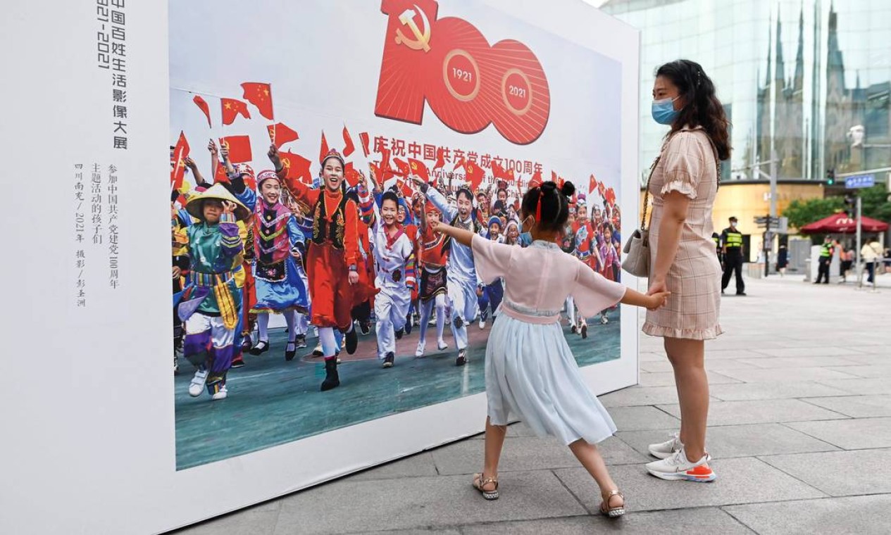 Uma mulher e uma criança visitam uma exposição de fotografia ao ar livre sobre os 100 anos do PCC, em uma rua comercial de Pequim Foto: WANG ZHAO / AFP