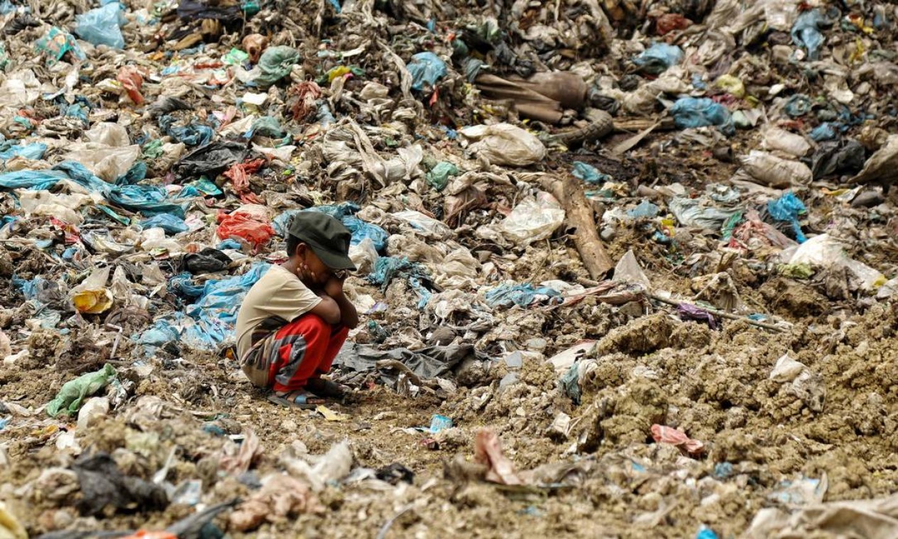 Criança aguarda o pai procurar por itens que possam ser revendidos em aterro sanitário em Alue Lim, em Lhokseumawe, Indonésia Foto: AZWAR IPANK / AFP