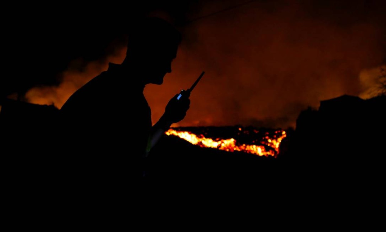 A lava flui ao lado de um policial local após a erupção de um vulcão no parque nacional Cumbre Vieja, em El Paso, nas ilhas Canárias Foto: BORJA SUAREZ / REUTERS