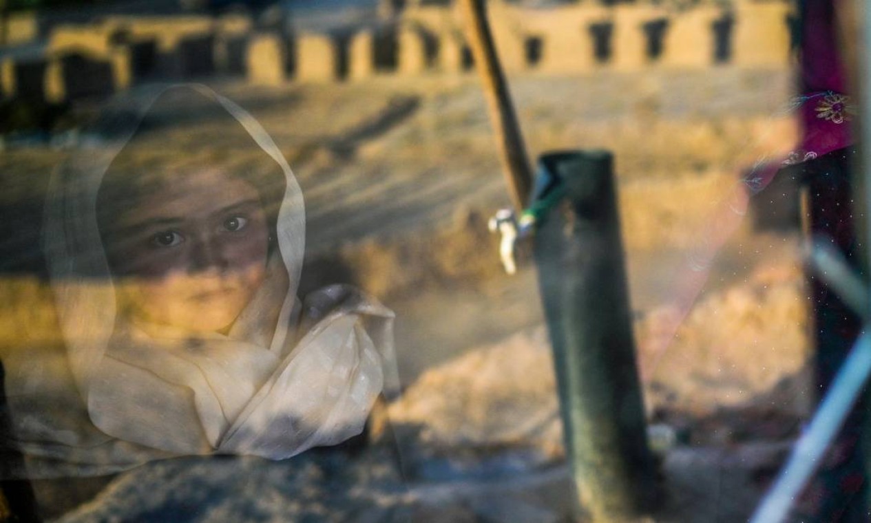 Garota da etnia Hazara é fotografada no reflexo da janela da sua caverna em um penhasco onde as pessoas ainda vivem como viviam séculos atrás em Bamiyan, no Afeganistão Foto: BULENT KILIC / AFP