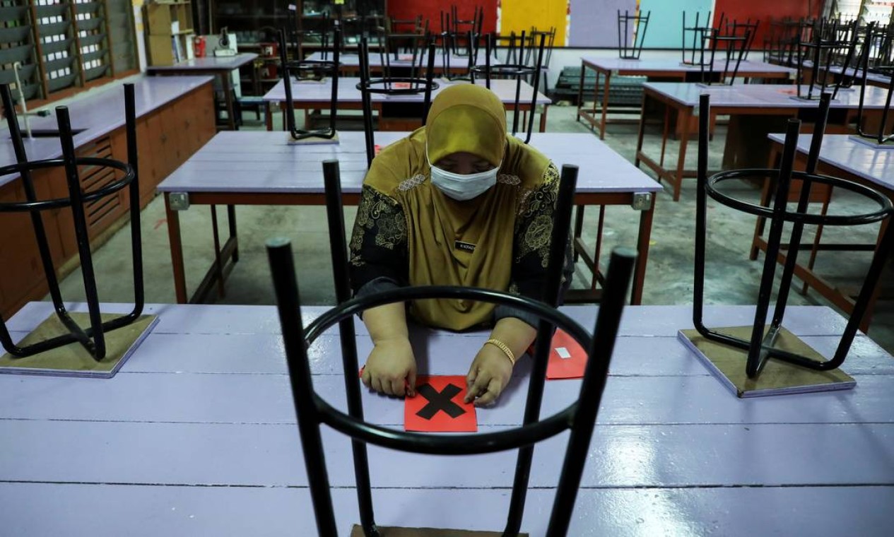 Professora marca uma mesa como parte das medidas de distanciamento social em uma escola secundária, em Kuala Lumpur, Malásia Foto: LIM HUEY TENG / REUTERS