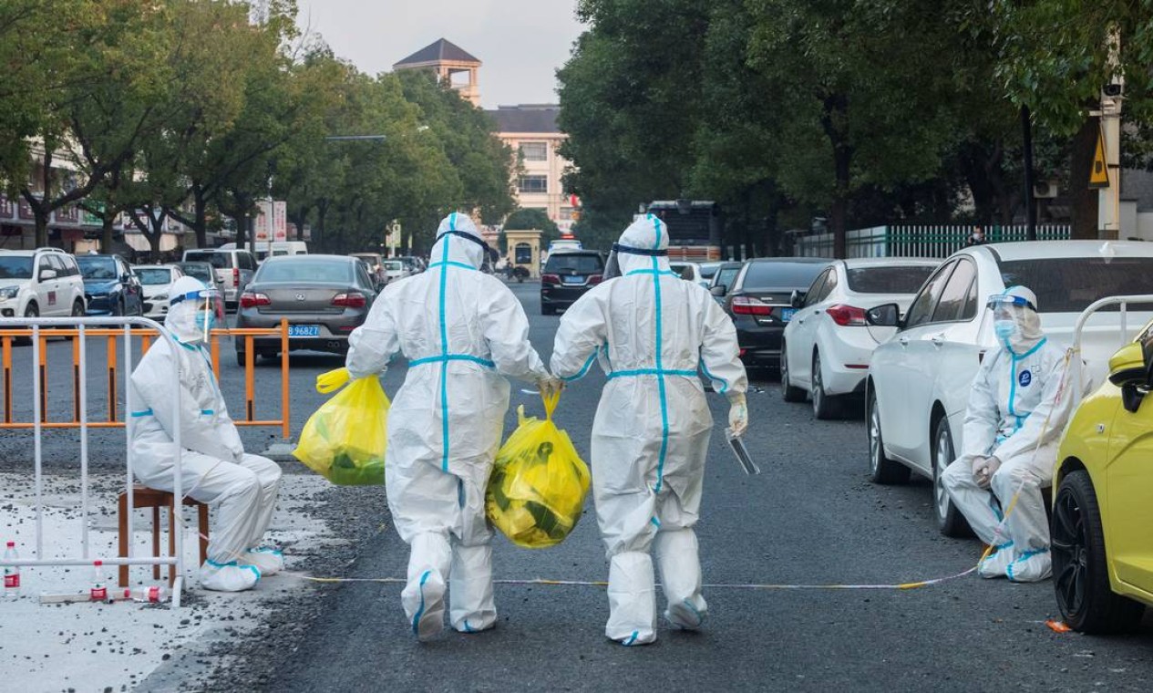 Trabalhadores em trajes de proteção carregam itens para residentes em um complexo fechado após novos casos da COVID-19, no distrito de Zhenhai de Ningbo, província de Zhejiang, China Foto: CHINA DAILY / VIA REUTERS