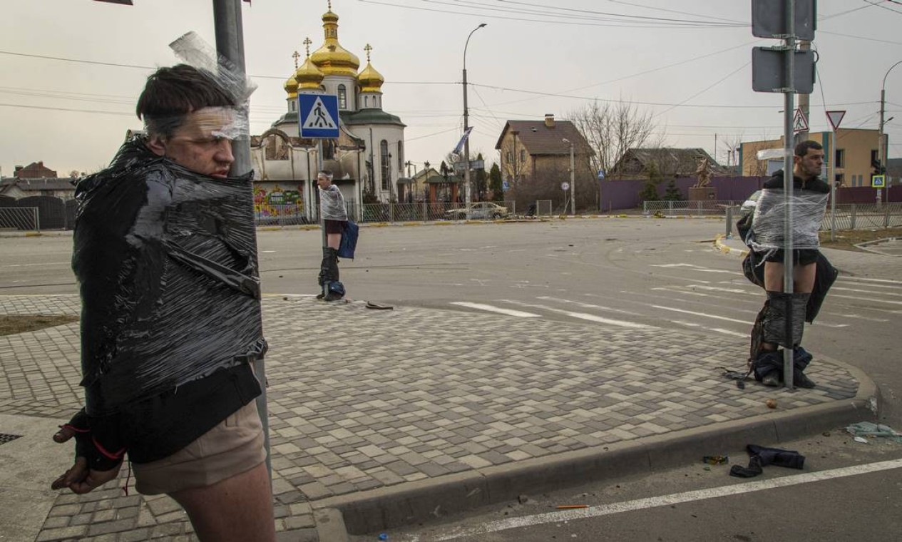 Os três homens acusados de roubar casas em Irpin e que foram exibidos na entrada da cidade no sábado Foto: YAN BOECHAT /  