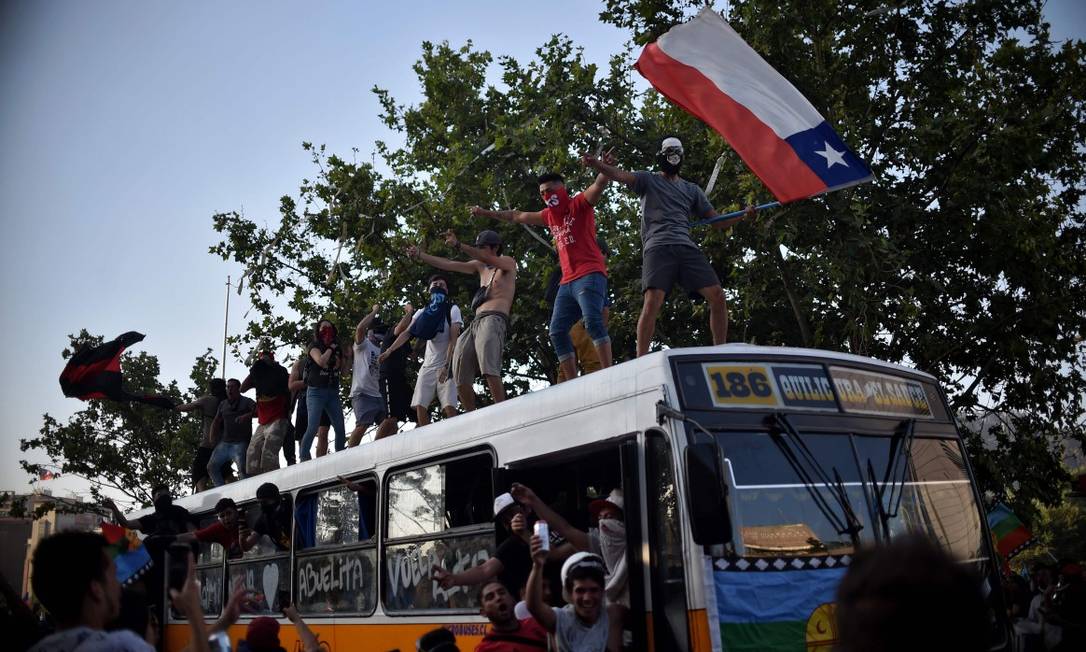 Manifestante balança bandeira do Chile em cima de ônibus durante protesto em Santiago Foto: RODRIGO ARANGUA / AFP 12-11-19