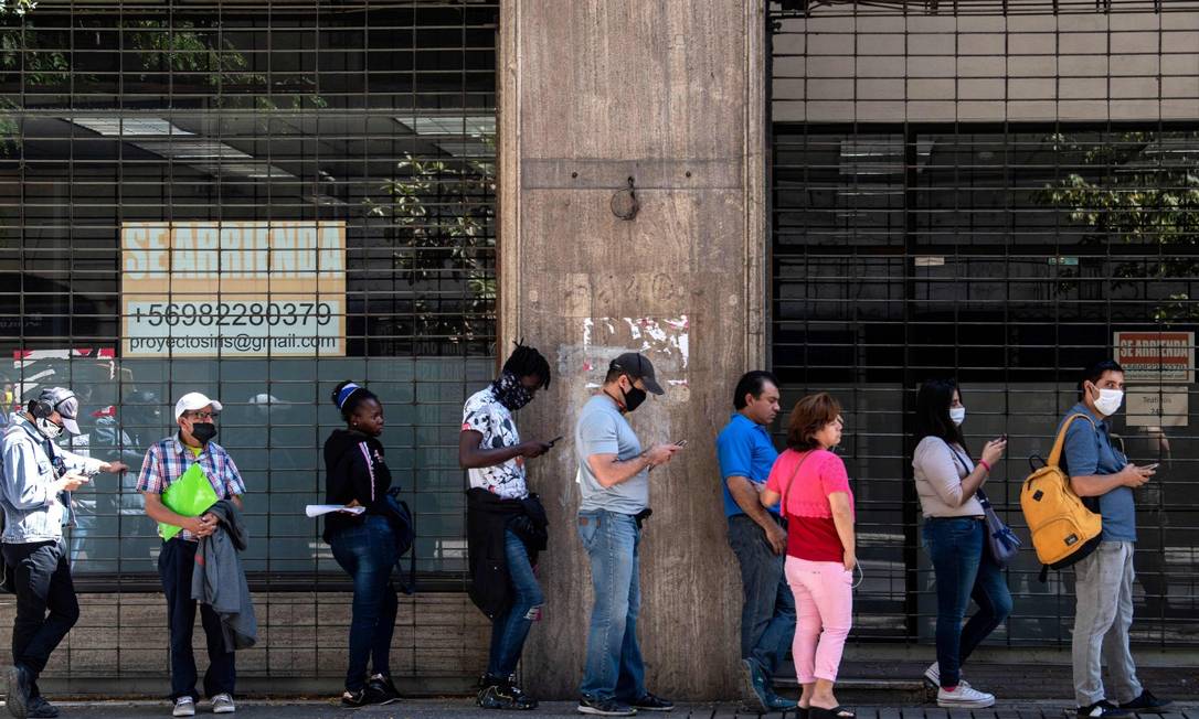 Pessoas usam máscara em fila para o recebe o auxílio-desemprego em Santiago Foto: MARTIN BERNETTI / AFP