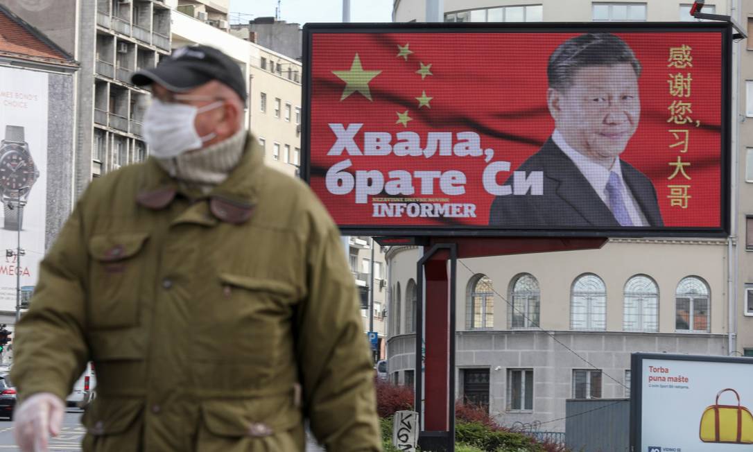 Homem de máscara em frente a outdoor com o presidente chinês Xi Jinping em Belgrado Foto: DJORDJE KOJADINOVIC / REUTERS