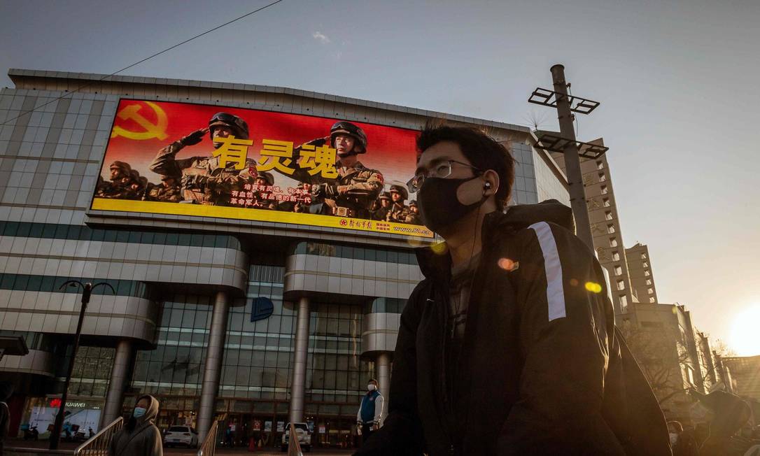Jovem usando máscara em frente a sinal de trânsito em Pequim Foto: NICOLAS ASFOURI / AFP