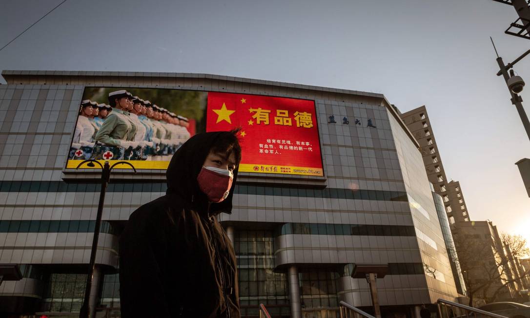 Um homem de máscara passa em frente a um outdoor com propaganda do Partido Comunista Chinês em Pequim Foto: NICOLAS ASFOURI / AFP