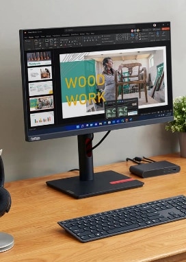 A collection of Lenovo products on a light-colored wooden desk including a ThinkVision monitor, ThinkPad laptop, and accessories.