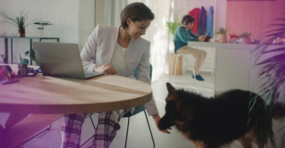 Woman sitting at a desk participating in a multi-party video call on a large screen Lenovo monitor.