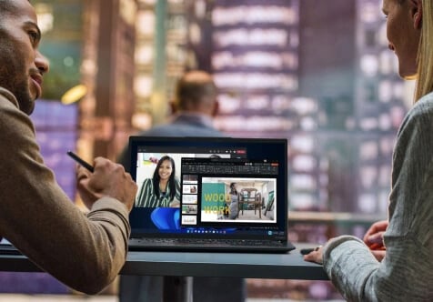 Two people at a desk talking over a Lenovo laptop.