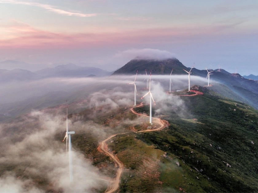 Windmills line a mountain road amid light fog.