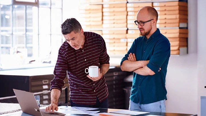 Two men at work looking at a laptop on a ping pong table