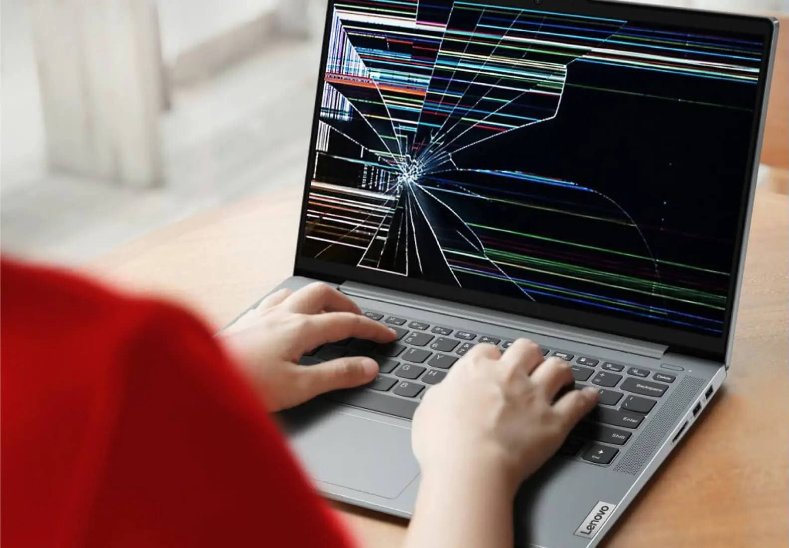 Three-quarters left-facing closeup of a Lenovo laptop with a cracked screen and fingers on the keyboard.