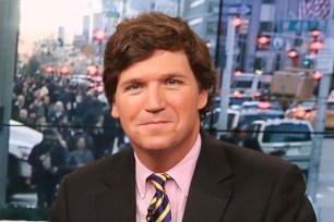 A headshot of Tucker Carlson wearing a dark jacket and striped tie in the Fox News studios in Midtown Manhattan/