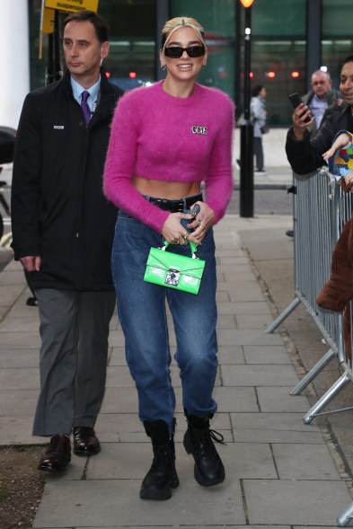 Dua Lipa wears a midriff sweater paired with high waisted jeans and a tiny green purse in London.