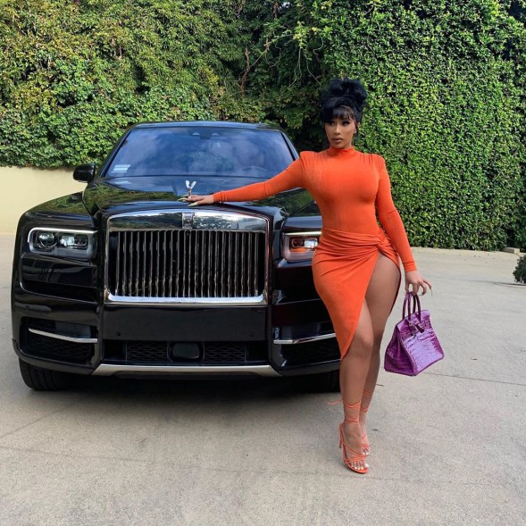 Cardi B shows some leg while posing with one of her many cars.