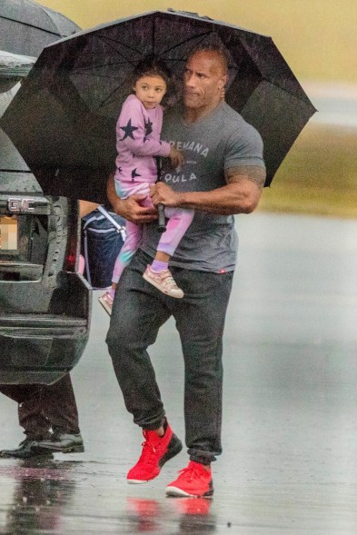 Dwayne "The Rock" Johnson braves the rain as he carries his little girl through the airport tarmac in Atlanta.