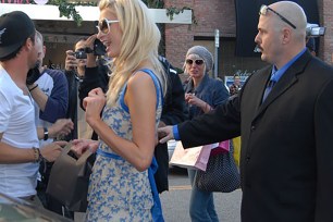 Bodyguard Kris Herzog walks behind Paris Hilton with his arm stretched out.