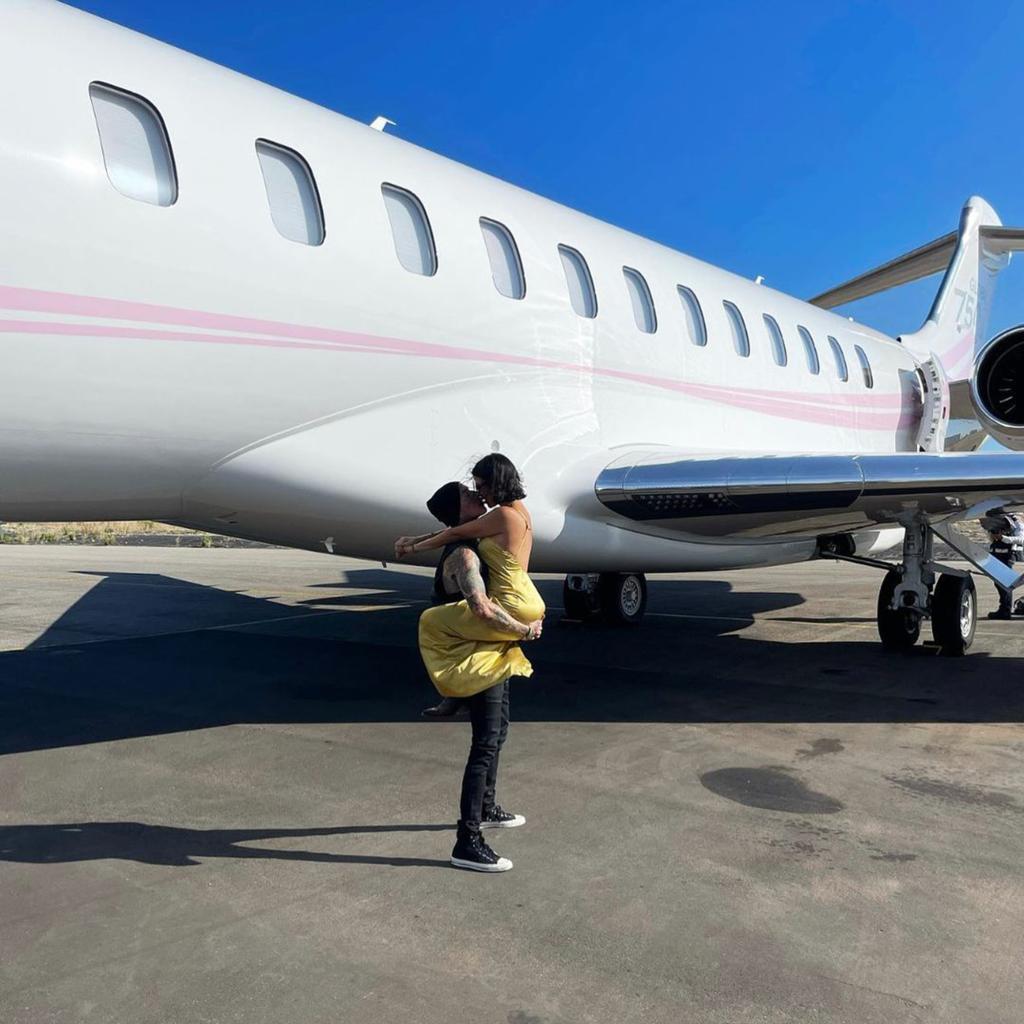 Kourtney Kardashian and Travis Barker in front of a private jet.