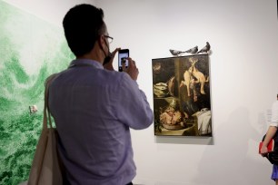 An Art Basel attendee taking a photo on his iPhone of artwork with taxidermied pigeons sitting on top.