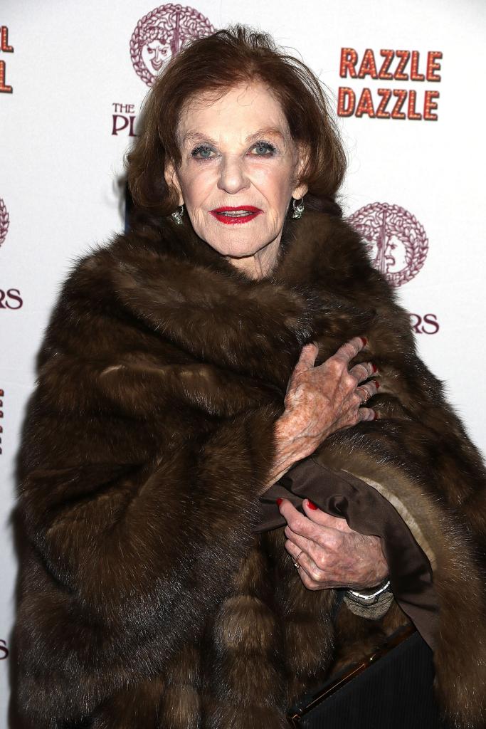 Joan Copeland standing on a red carpet in a fur coat.