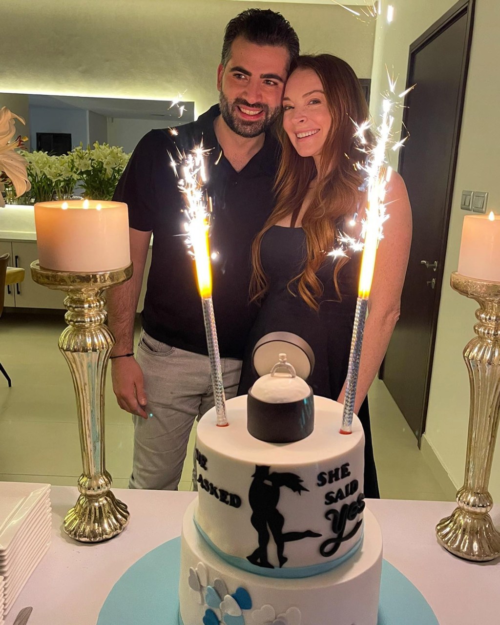 A photo of Lindsay Lohan and Bader Shammas posing behind their engagement cake